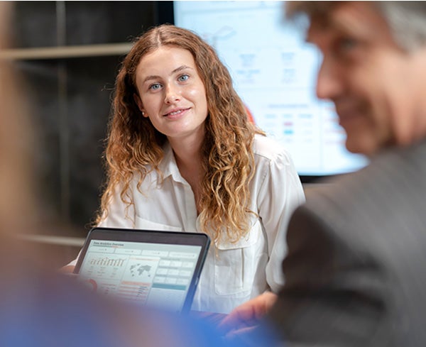 A smiling woman sitting near a window with a laptop surrounded by greenery