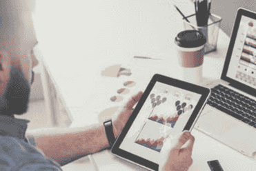 A professional reviewing financial data and charts on a tablet and laptop.