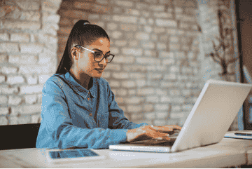 A young woman in glasses working on a laptop at a modern workspace.