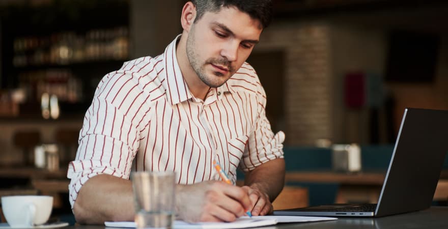 Adult man sitting in a cafe taking notes on an assignment for his masters degree.