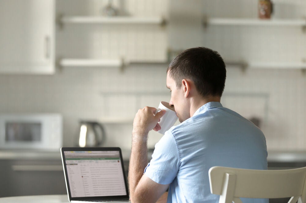 A university student sips coffee while studying at home.