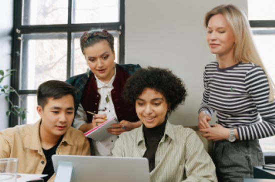 Postgraduate students huddled around a student with a laptop.