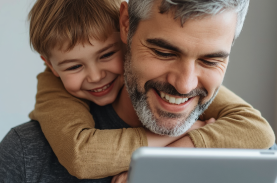 A man and a child are smiling and looking at a tablet together.