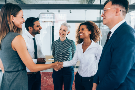 A group of business people shaking hands and smiling in an office setting.