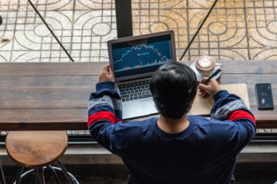 From above, a student sits with a coffee and his laptop researching fintech courses in Australia