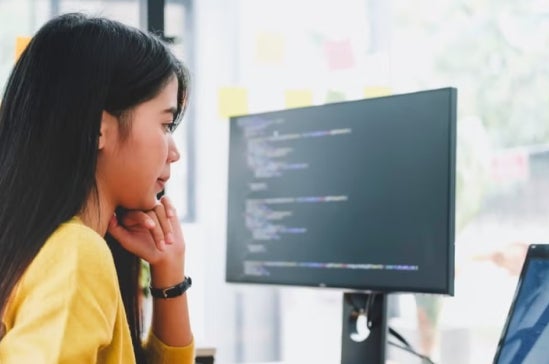 A data scientist studies code on a laptop and computer monitor.