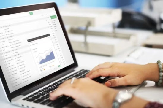 Hands typing on a laptop keyboard with an email inbox open on screen, displaying a data chart, representing digital analytics or data review.