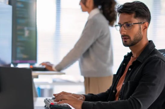 A cybersecurity analyst with eyeglasses working on a laptop.
