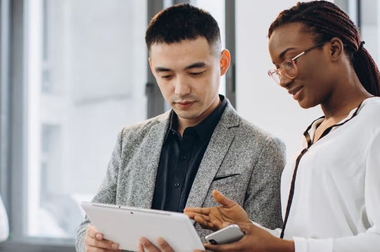 Two professionals, one man and one woman, review a tablet together in a bright office, illustrating discussion about cybersecurity and technology teamwork.