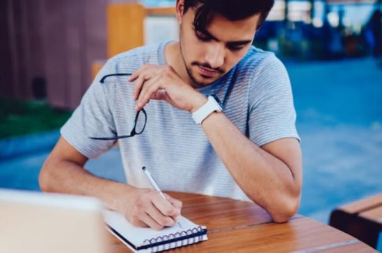 A postgraduate student writing revision notes in a notepad