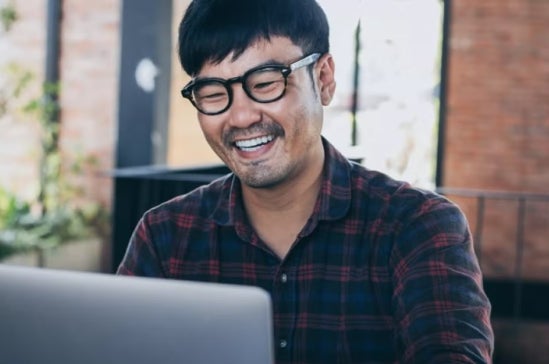 Man in glasses and a plaid shirt works on a laptop in a casual, modern work environment, conveying real-world financial application.