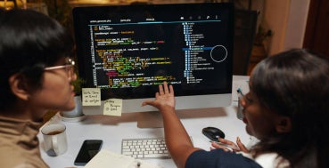 Two data professionals discussing programming code on a monitor.