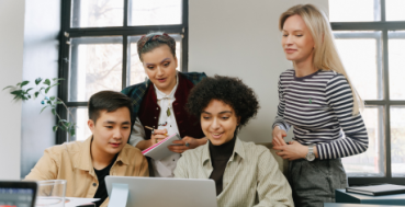 Postgraduate students huddled around a student with a laptop.