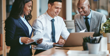 Three professionals in business attire collaborating around a laptop at a desk.