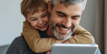 A man and a child are smiling and looking at a tablet together.