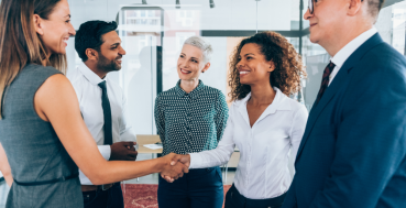 A group of business people shaking hands and smiling in an office setting.