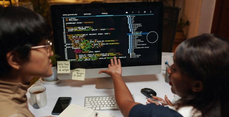 Two data professionals discussing programming code on a monitor.