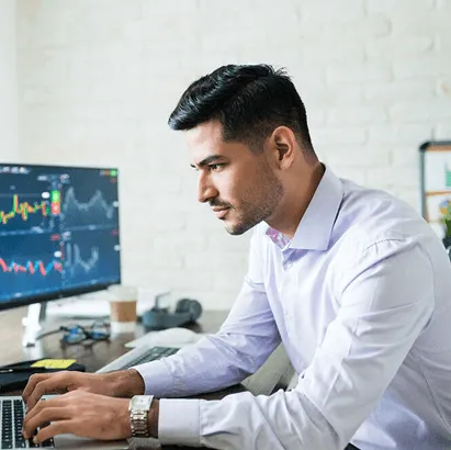Professional working at a desk with data charts displayed on a computer screen.