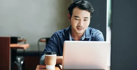 Professional woman in a suit smiles while sitting by tall office windows, suggesting confidence and optimism in a modern workplace.