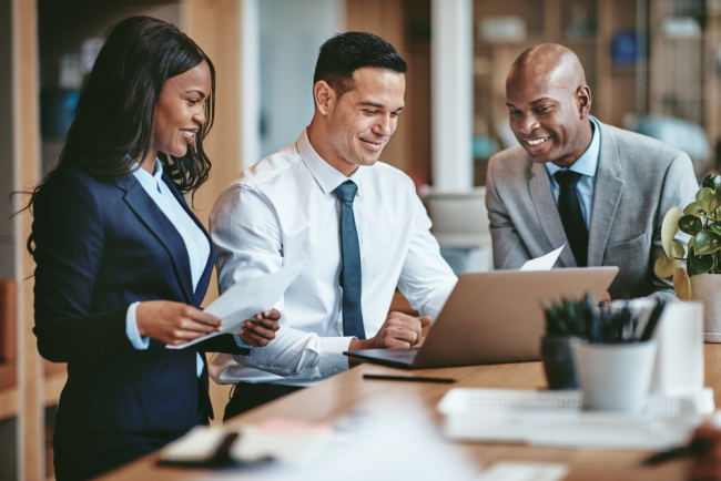 Three professionals in business attire collaborating around a laptop at a desk.