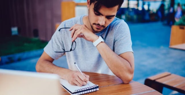 A postgraduate student writing revision notes in a notepad