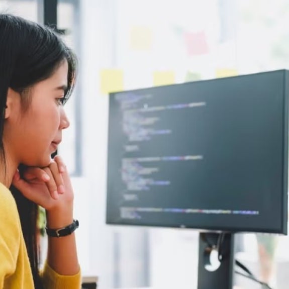 A data scientist studies code on a laptop and computer monitor.