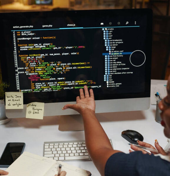 Two data professionals discussing programming code on a monitor.