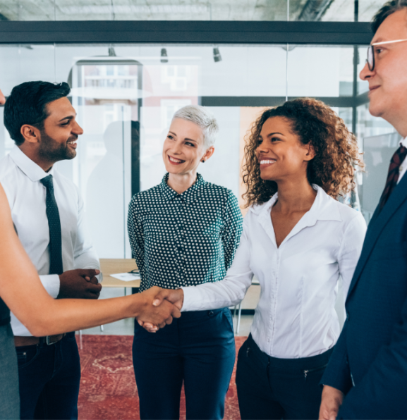 A group of business people shaking hands and smiling in an office setting.