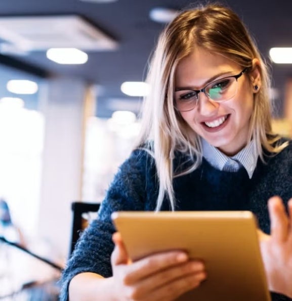 Woman with long blonde hair uses a tablet in a modern cafe or workspace, illustrating participation and advancement of women in the finance sector.