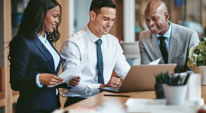 Three professionals in business attire collaborating around a laptop at a desk.