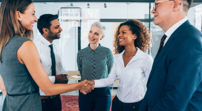 A group of business people shaking hands and smiling in an office setting.