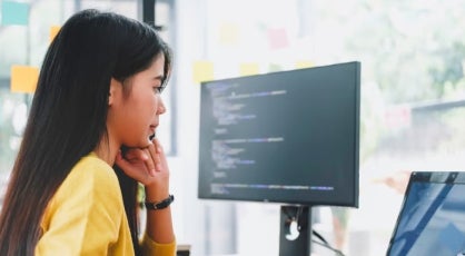 A data scientist studies code on a laptop and computer monitor.