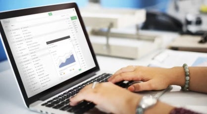 Hands typing on a laptop keyboard with an email inbox open on screen, displaying a data chart, representing digital analytics or data review.