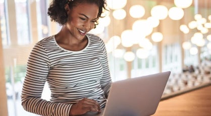 Woman in a striped shirt using a laptop in a brightly lit room, suggesting online research or studying financial aid options.