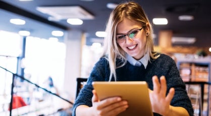 Woman with long blonde hair uses a tablet in a modern cafe or workspace, illustrating participation and advancement of women in the finance sector.