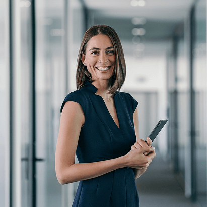 Professional standing in an office corridor holding a mobile device.
