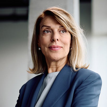 A middle-aged woman in a business suit smiling and looking out the window.
