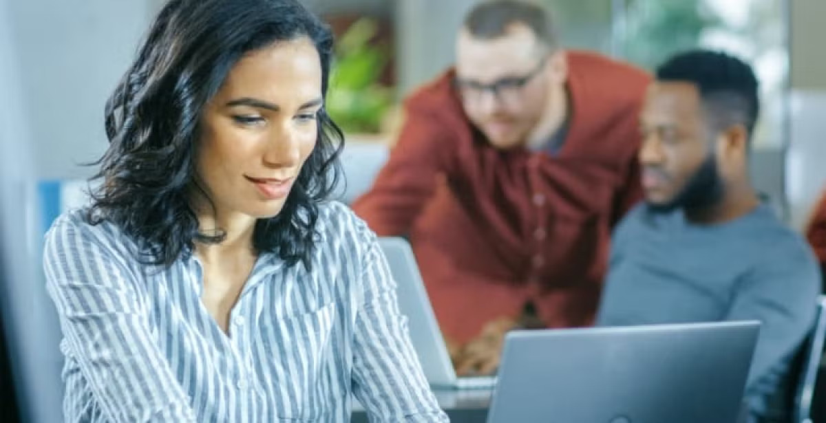 A student works on a laptop in a group study session, with classmates and laptops visible, reflecting collaboration and time management in an academic setting.