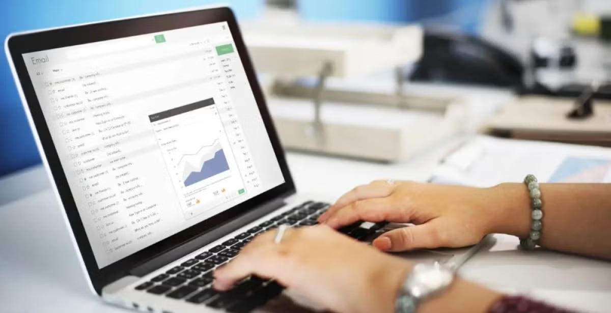 Hands typing on a laptop keyboard with an email inbox open on screen, displaying a data chart, representing digital analytics or data review.