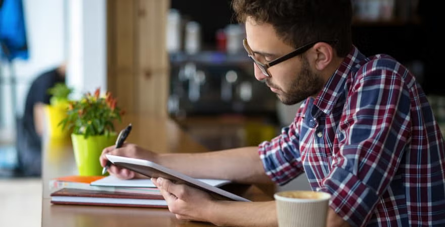 A man is seated at a table, diligently writing notes in a notebook.