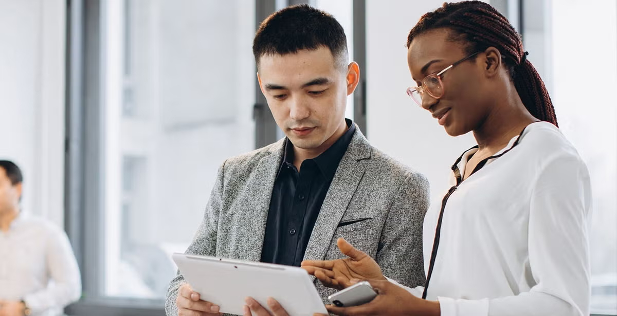 Two professionals, one man and one woman, review a tablet together in a bright office, illustrating discussion about cybersecurity and technology teamwork.