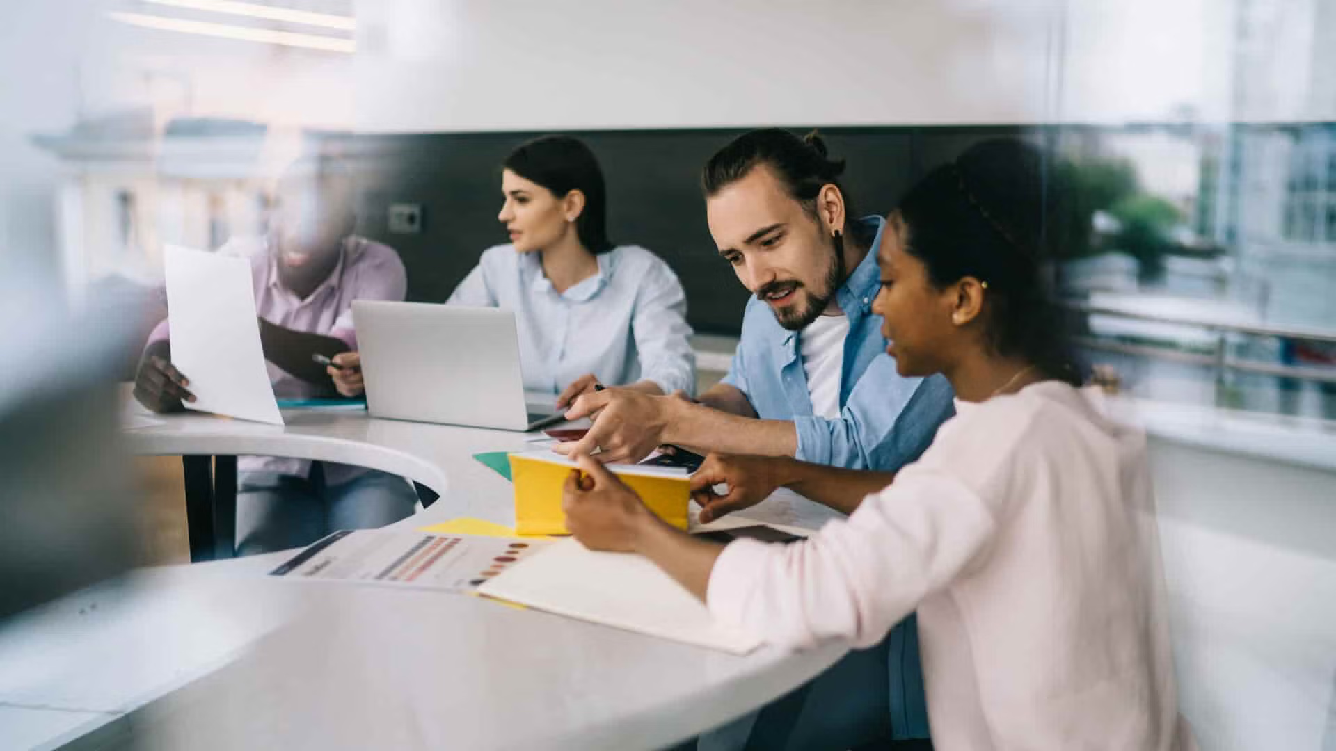 A diverse group of cyber security professionals collaborating on laptops in a modern office setting.