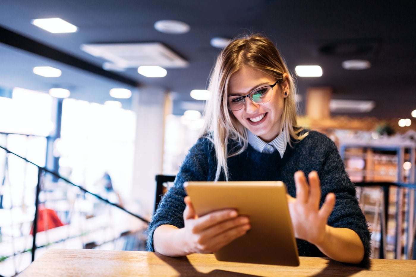 A woman with glasses scrolling on her tablet.